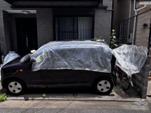車と壁の隙間に置いた自転車にビニール袋のカバーをかけた様子