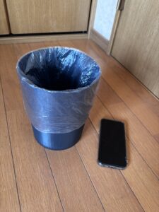 夫の部屋の100均の小さなゴミ箱。半透明の袋を掛けてスマホと大きさ比較